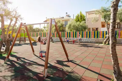 a child playing on a swing set in a playground at Sirios Village Hotel & Bungalows - All Inclusive in Kato Daratso