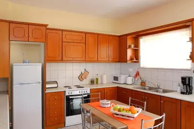 a kitchen with wooden cabinets and a table with a bowl of fruit at Sofoklis Apts in Stalos