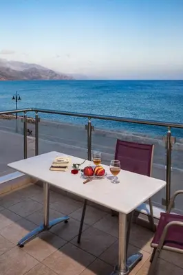 a table with two glasses of wine on a balcony with the ocean at Paleochora Apartments in Palaiochóra