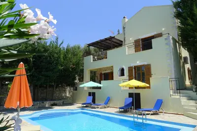 a swimming pool with chairs and umbrellas next to a house at Villa Rodi in Gavalochori