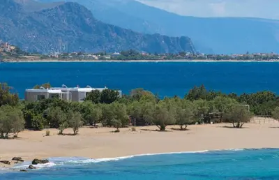 a beach with a building in the middle of the water at Cedar Bay Beachside Villas in Palaiochóra