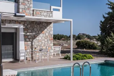 a patio with a table and chairs next to a swimming pool at Cedar Bay Beachside Villas in Palaiochóra