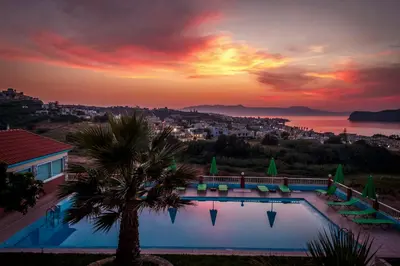 a sunset over a swimming pool with a palm tree at Eliros Studios in Stalos