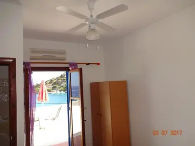 a ceiling fan in a room with a door to a beach at Scirocco Rooms in Loutro