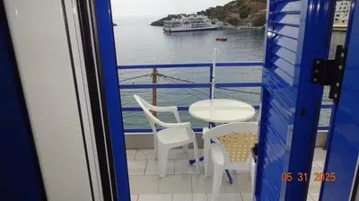 a balcony with a table and chairs and a boat in the water at Scirocco Rooms in Loutro