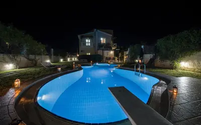 a large blue swimming pool at night at Villa Ifigeneia Private Hot Tub Rooms in Kalathas