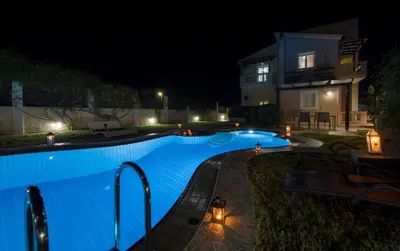 a swimming pool in front of a house at night at Villa Ifigeneia Private Hot Tub Rooms in Kalathas