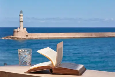 a book on a table with a glass and a lighthouse at Domus Renier Boutique Hotel in Chania Town