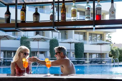 a man and woman are holding drinks in a pool at Thalassa Beach Resort & Spa (Adults Only) in Agia Marina Nea Kydonias