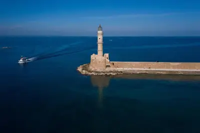 a lighthouse in the middle of the water with a boat at San Salvatore Monastery in Chania Town