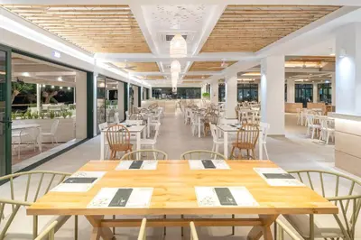 a restaurant with wooden tables and chairs and windows at Iolida Beach by Smile Hotels in Agia Marina Nea Kydonias