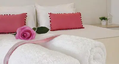 a bed with pink and white pillows and a pink rose at Crown Apartments in Kalyves