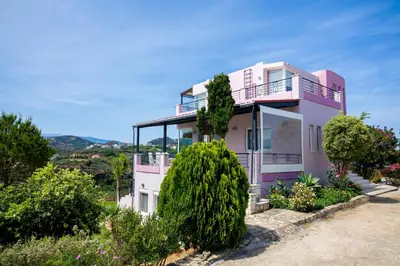 a pink house with a balcony and trees at Villa Anatoli in Stalos