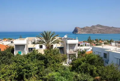 a building with a palm tree in front of the ocean at Manias Hotel Apartments in Agia Marina Nea Kydonias