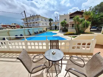 a balcony with chairs and a table and a pool at Perla Beach in Agia Marina Nea Kydonias