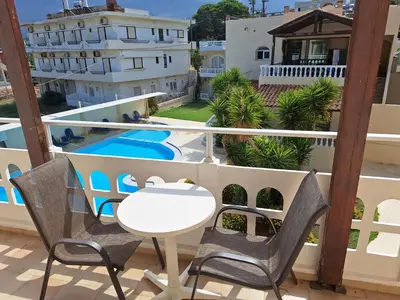 a balcony with a table and chairs and a swimming pool at Perla Beach in Agia Marina Nea Kydonias