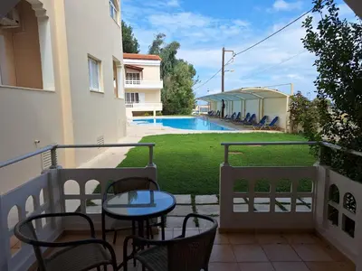 a balcony with a table and chairs and a swimming pool at Perla Beach in Agia Marina Nea Kydonias
