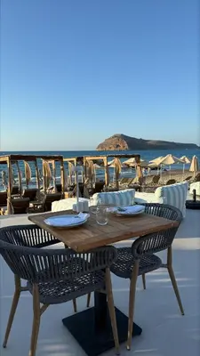 a wooden table and chairs on a patio with the ocean at Τhe Noverian Antama Organic Beach Resort Chania with Outdoor Heated Pool in Agia Marina Nea Kydonias