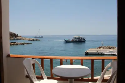 a balcony with two chairs and a boat in the water at Hotel Alkyon in Khóra Sfakíon