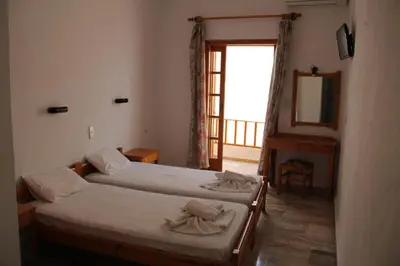 two beds in a room with a window and a mirror at Hotel Alkyon in Khóra Sfakíon