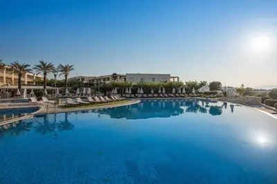 a large blue swimming pool with chairs and palm trees at Cretan Dream Resort & Spa in Stalos