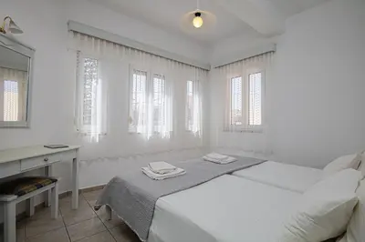 a white bedroom with a bed and a desk and windows at Marias Studios & Apartments in Platanias in Plataniás
