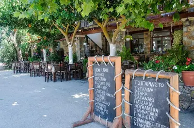 a sign in front of a restaurant with tables and chairs at Platanos Rooms in Anopoli Sfakion