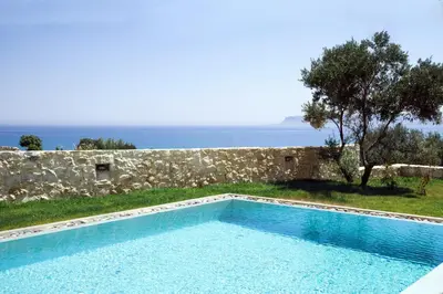 a swimming pool in front of a stone wall at Iskios Villas in Agia Marina Nea Kydonias