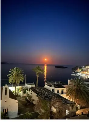 a sunset over the water with palm trees and buildings at Loutro Holidays in Loutro