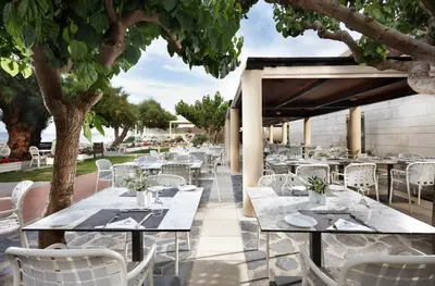 a restaurant with white tables and chairs under a tree at Giannoulis – Santa Marina Beach Hotel in Agia Marina Nea Kydonias