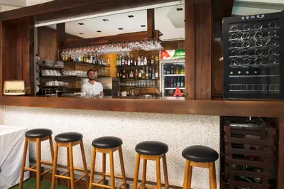 a man standing behind a bar with stools at Talos Hotel Apartments in Kato Daratso