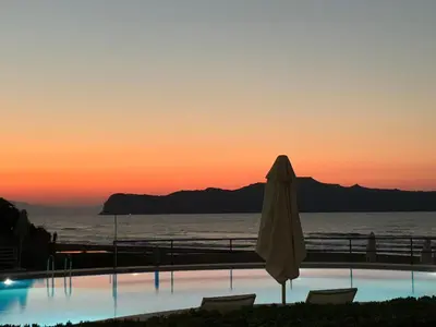 an umbrella and chairs next to a swimming pool with the sunset at Phaedra Hotel in Stalos