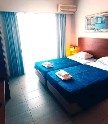 a bedroom with two beds with blue sheets and a window at Bella Pais in Maleme
