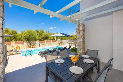 a patio with a table and chairs and a pool at Villa Tzina in Plataniás
