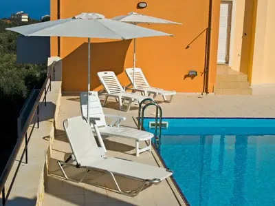 a group of chairs and an umbrella next to a pool at Olive Tree Hillside Apartment in Stalos