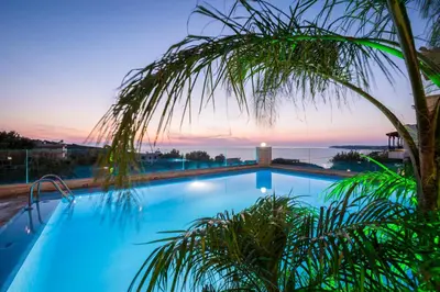 a swimming pool with a palm tree in front of a sunset at Esplanade Apartments - Heated Pool in Kalathas