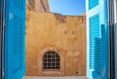 a window in the side of a building with blue shutters at Lucia Hotel in Chania Town