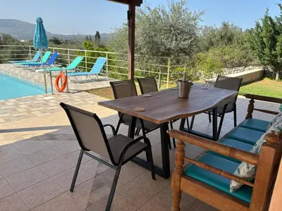 a wooden table and chairs on a patio with a pool at Villa Adriana in Arménoi