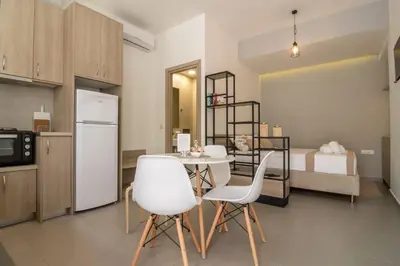 a kitchen with a table and white chairs and a bed at AnDi's Apartment's Paleochora in Palaiochóra