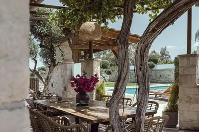 a table and chairs under a wooden pergola with a pool at Antonia Blue Villa in Mourniaí