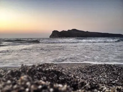 a beach with a mountain in the ocean with waves at Michael Apartments in Agia Marina Nea Kydonias
