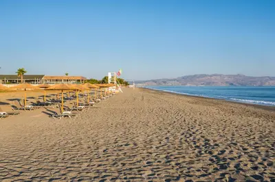 a beach with chairs and umbrellas and the ocean at Hotel Caretta Beach in Gerani Chanion