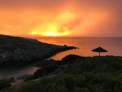 a sunset over the ocean with umbrellas on a beach at Giorgi's Blue Apartments in Kalathas