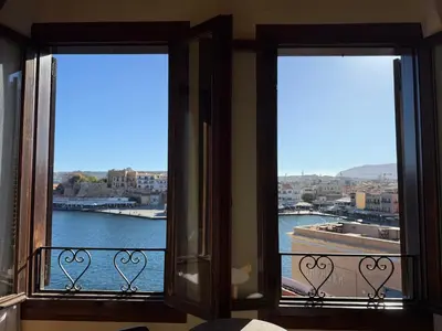 two windows in a room with a view of the water at Helena Hotel in Chania Town
