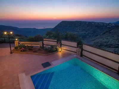 a swimming pool with two benches and a sunset at Falasarna Villas in Falasarna