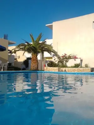 a swimming pool with a palm tree in front of a building at Karmi Apartments in Kolymvari