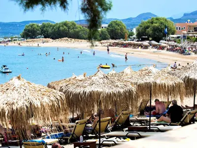 a beach with people in the water and straw umbrellas at Aphrodite Beach in Kissamos
