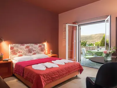 a bedroom with a bed with a red blanket and a balcony at Petritos Rooms and Studios in Falasarna