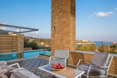 a patio with two chairs and a table with a bowl of fruit at Olea Villas - Infinity Pool, Hot Tub, Sea Views in Marathi