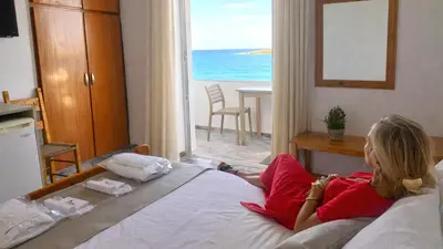 a woman laying on a bed looking out a window at Klinakis Beach Hotel in Chania Town